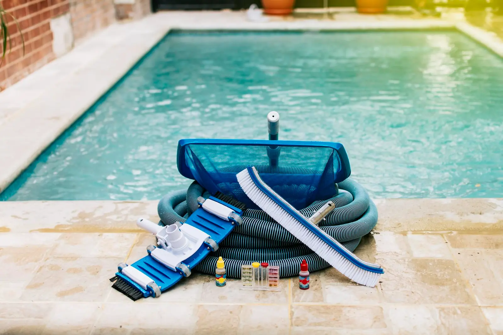 Pool cleaning equipment including net, vacuum, hoses and brushes arranged on pool deck by clear blue water - Cox Pool Services & Repair, Clovis, CA