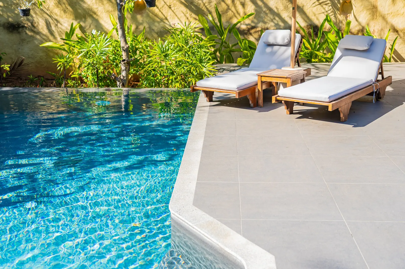 Crystal-clear blue pool with clean tile deck, lounge chairs, and tropical plants in bright sunlight - Cox Pool Services & Repair, Clovis, CA