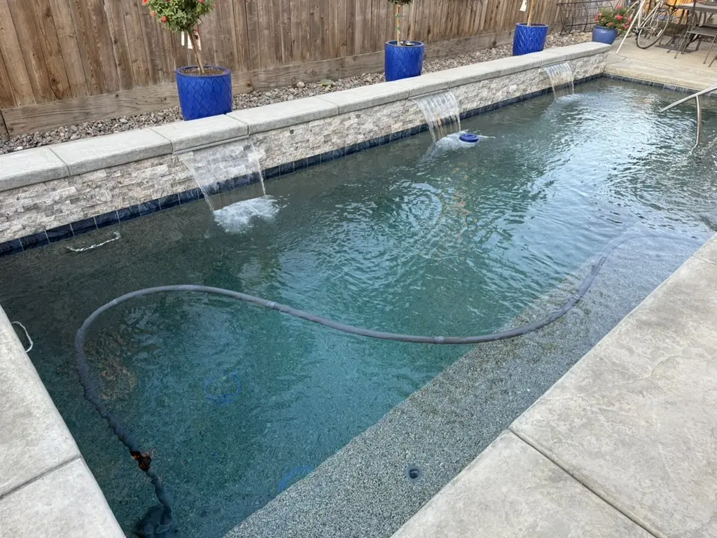 Clear blue-green pool with stone coping, decorative tile stripe, and water features in a landscaped backyard - Pine Ridge Pool Care, Inc., Clovis, CA