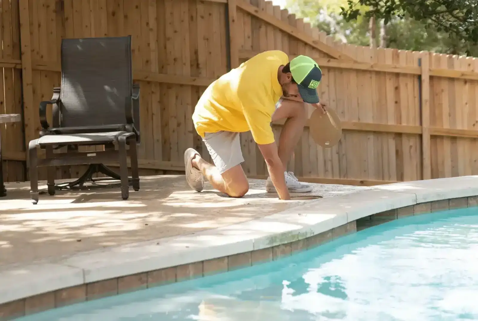 Technician in yellow shirt and cap kneeling by a bright blue pool, performing maintenance work on the deck - Pool Doctor, Cape Coral, FL