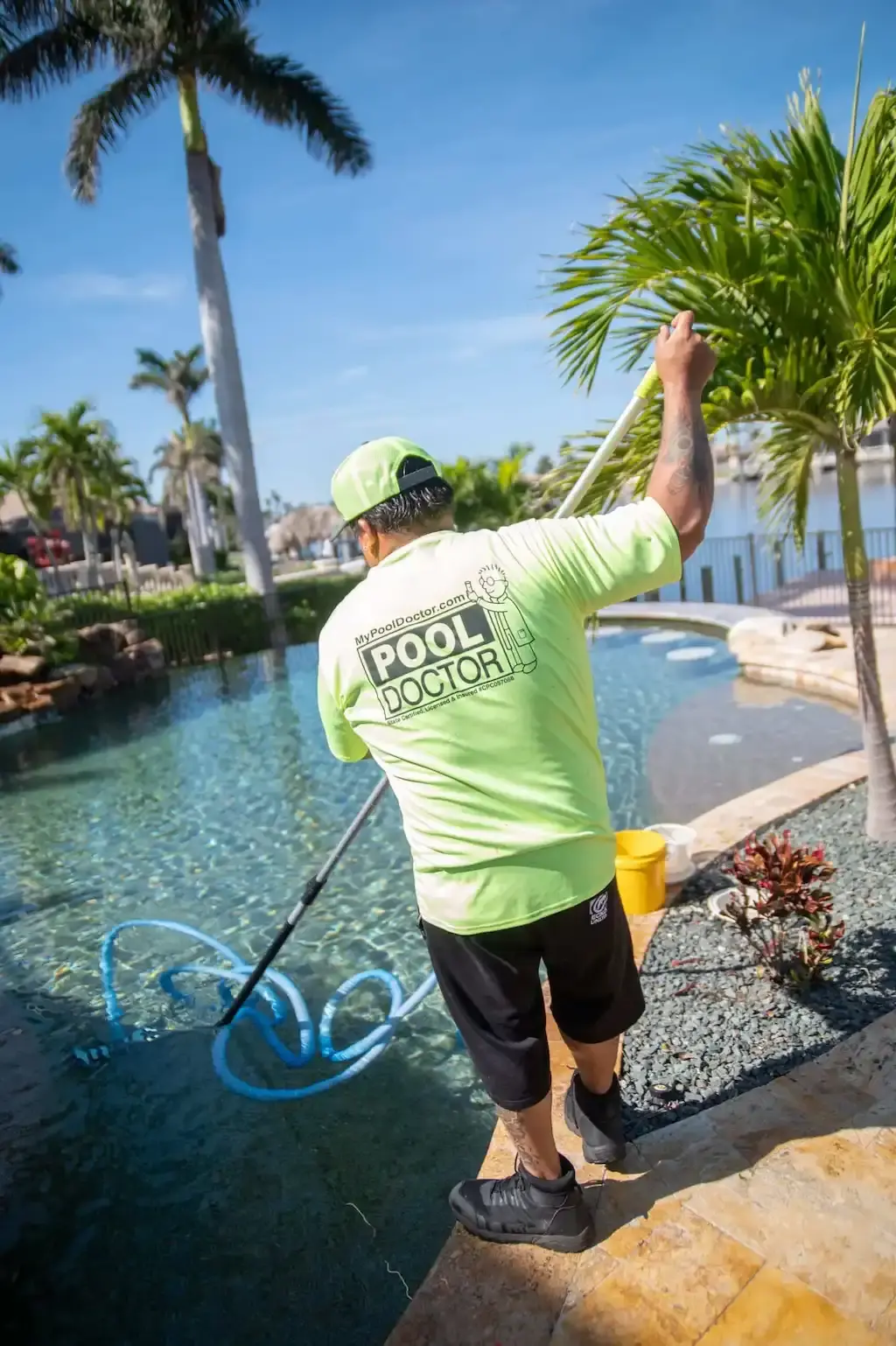 Pool Doctor technician in branded neon shirt working at a bright blue residential pool - Pool Doctor, Cape Coral, FL