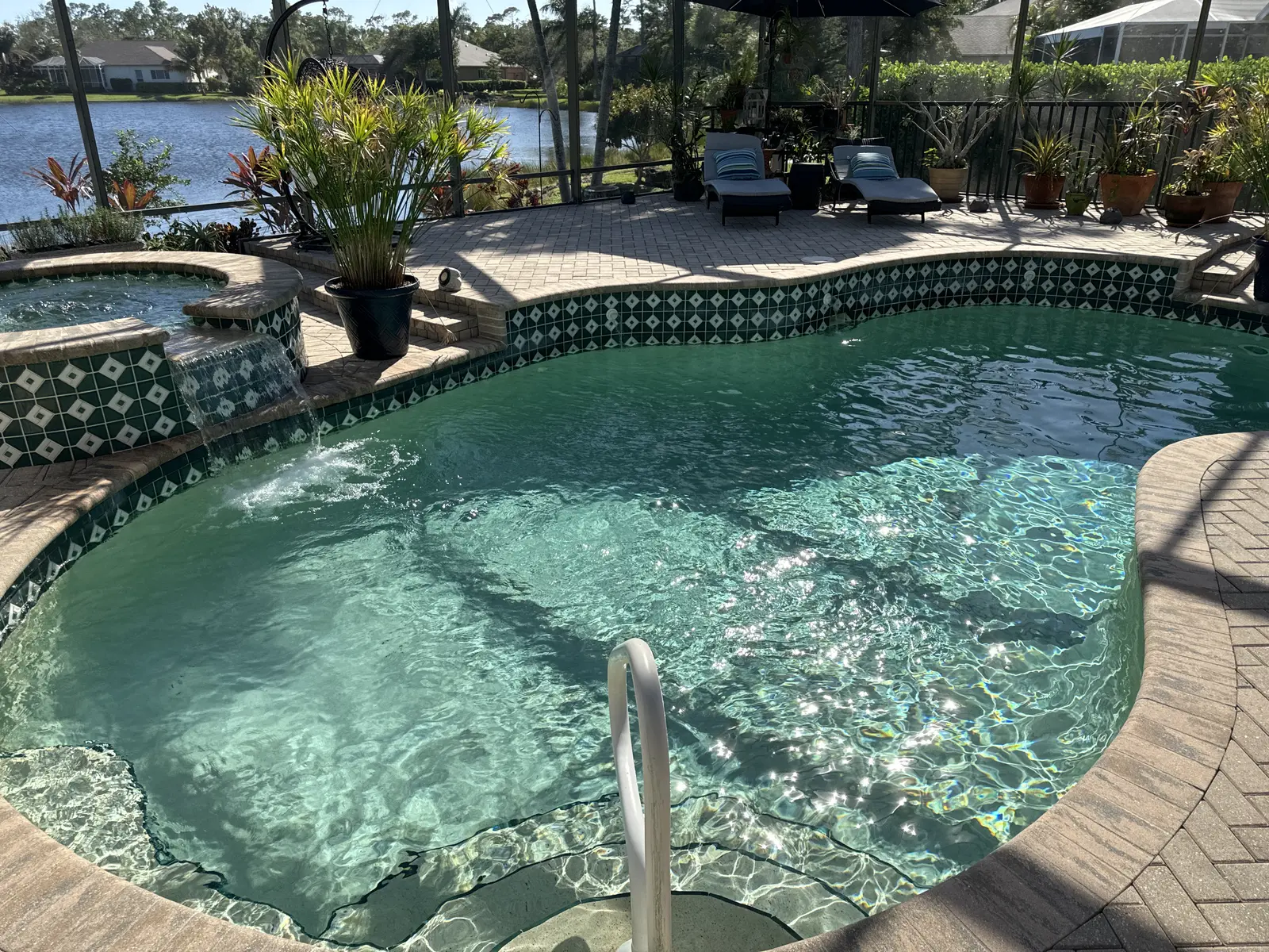 Crystal clear turquoise pool with decorative tile border and spa, surrounded by patio and waterfront view - Pool Doctor, Cape Coral, FL