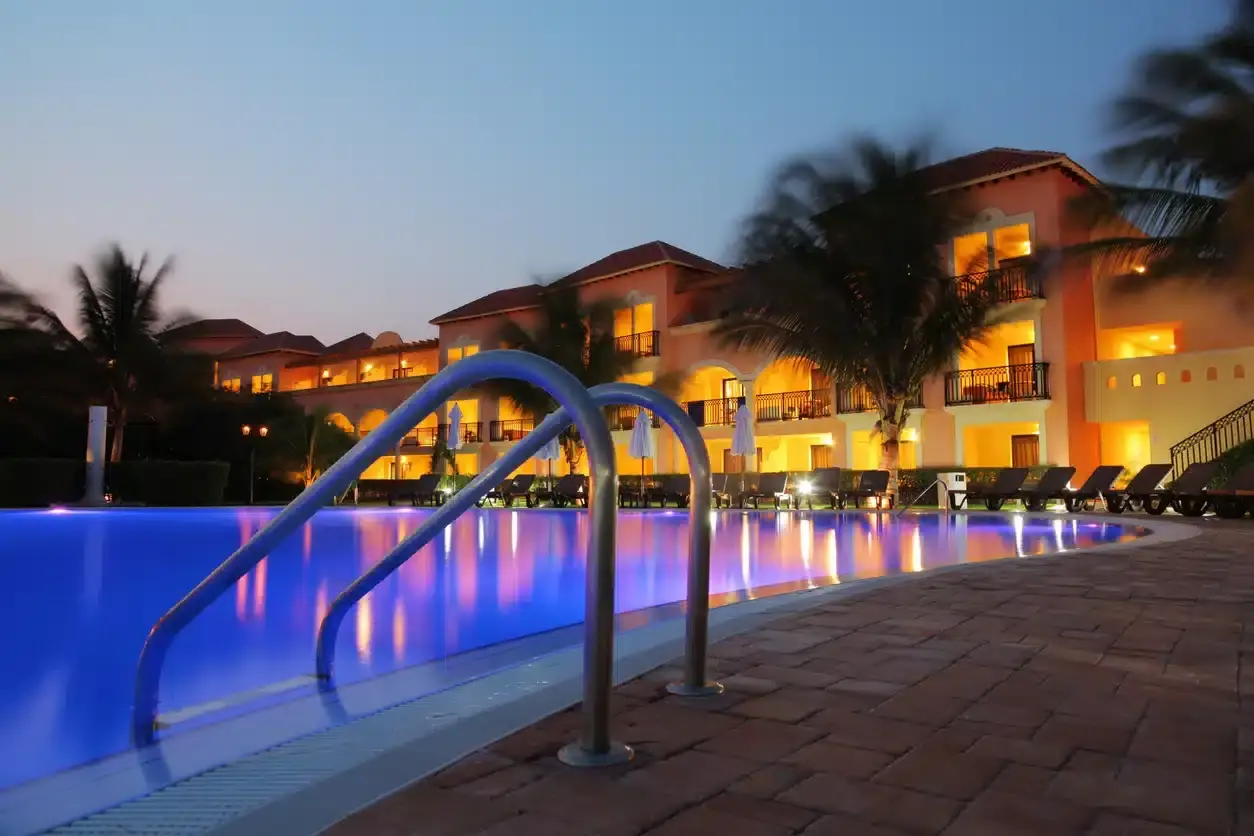 Illuminated resort pool with blue water and metal handrails at dusk, resort buildings lit in background - Pool Doctor, Cape Coral, FL