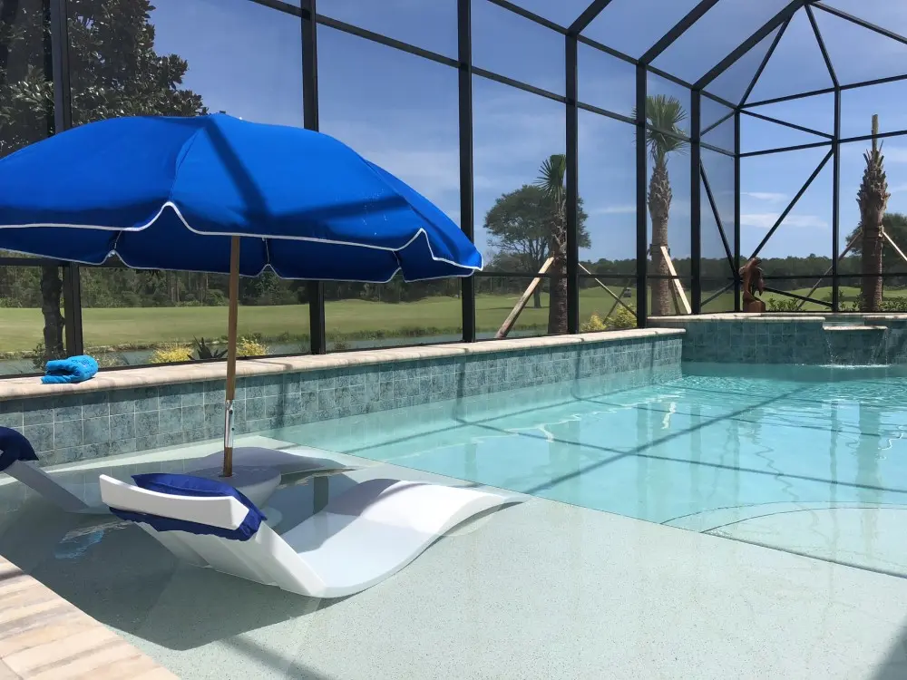 A crystal-clear swimming pool with blue umbrella, lounge chair, and screened enclosure overlooking a golf course - Coastal Luxury Outdoors, Jacksonville, FL