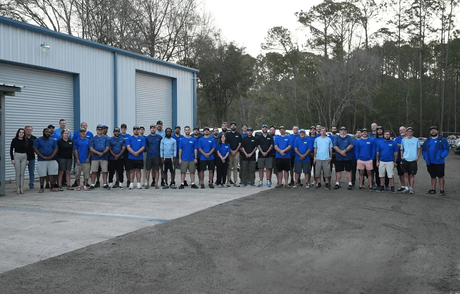 Large team of pool service employees wearing blue uniforms standing together in front of company facility - Jomo Pool Service, Jacksonville, FL