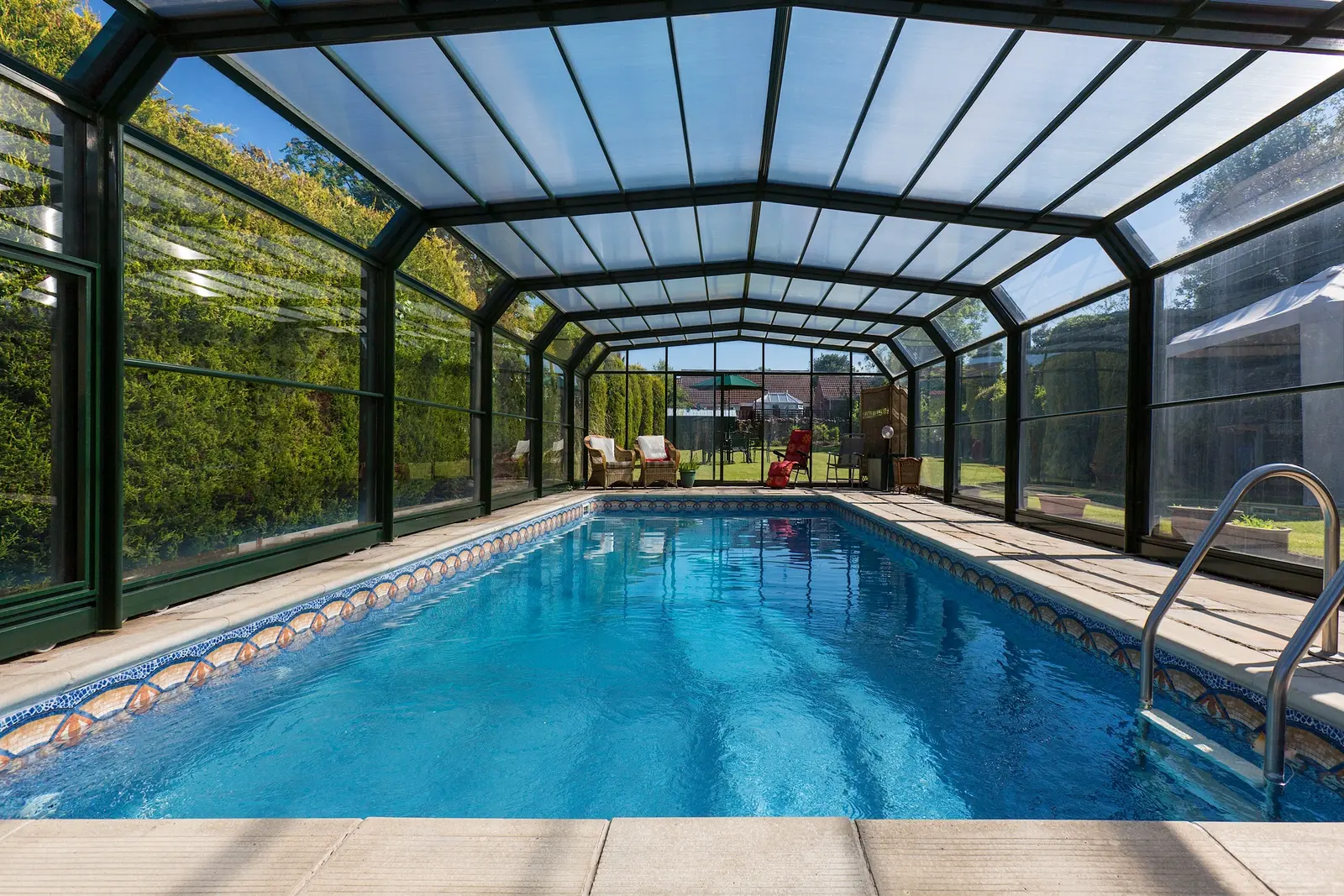 Crystal-clear indoor swimming pool under glass enclosure with decorative tile border and metal railings - North East Florida Pool Service, Jacksonville, FL