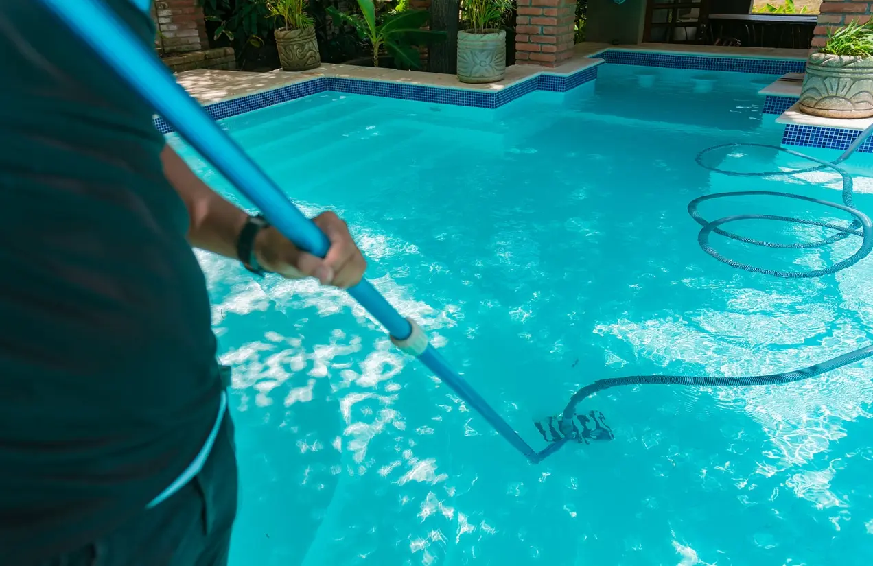 Technician cleaning a bright turquoise pool with equipment and hoses visible - Patriot Pool & Spa Formerly (Magnolia Pool and Spa), Naples, FL