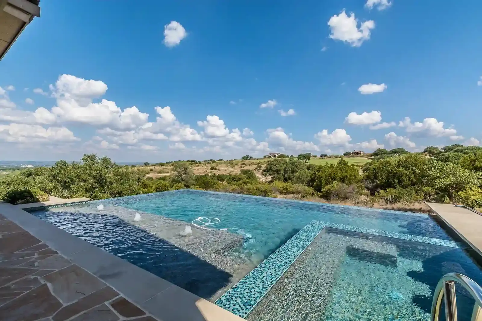 Crystal-clear swimming pool with decorative tile work overlooking rolling green hills and blue sky - Patriot Pool & Spa Formerly (Magnolia Pool and Spa), Naples, FL