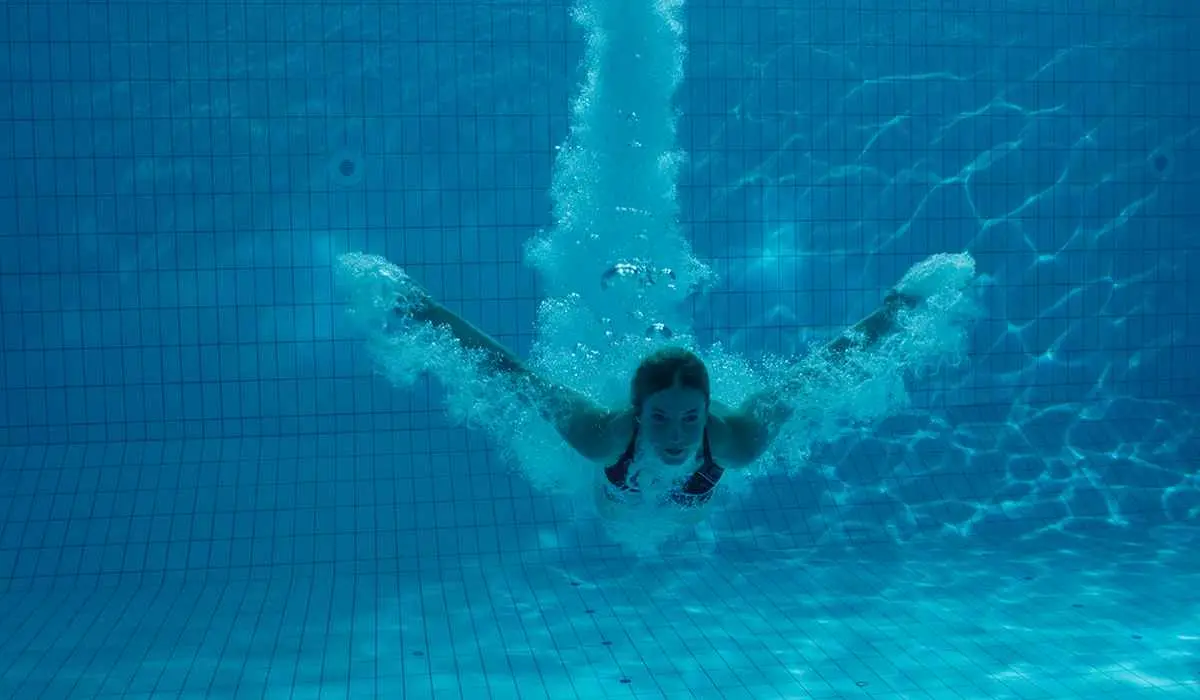 Child doing butterfly stroke underwater in a bright blue tiled swimming pool - Blue Science Pool Service, Tampa, FL
