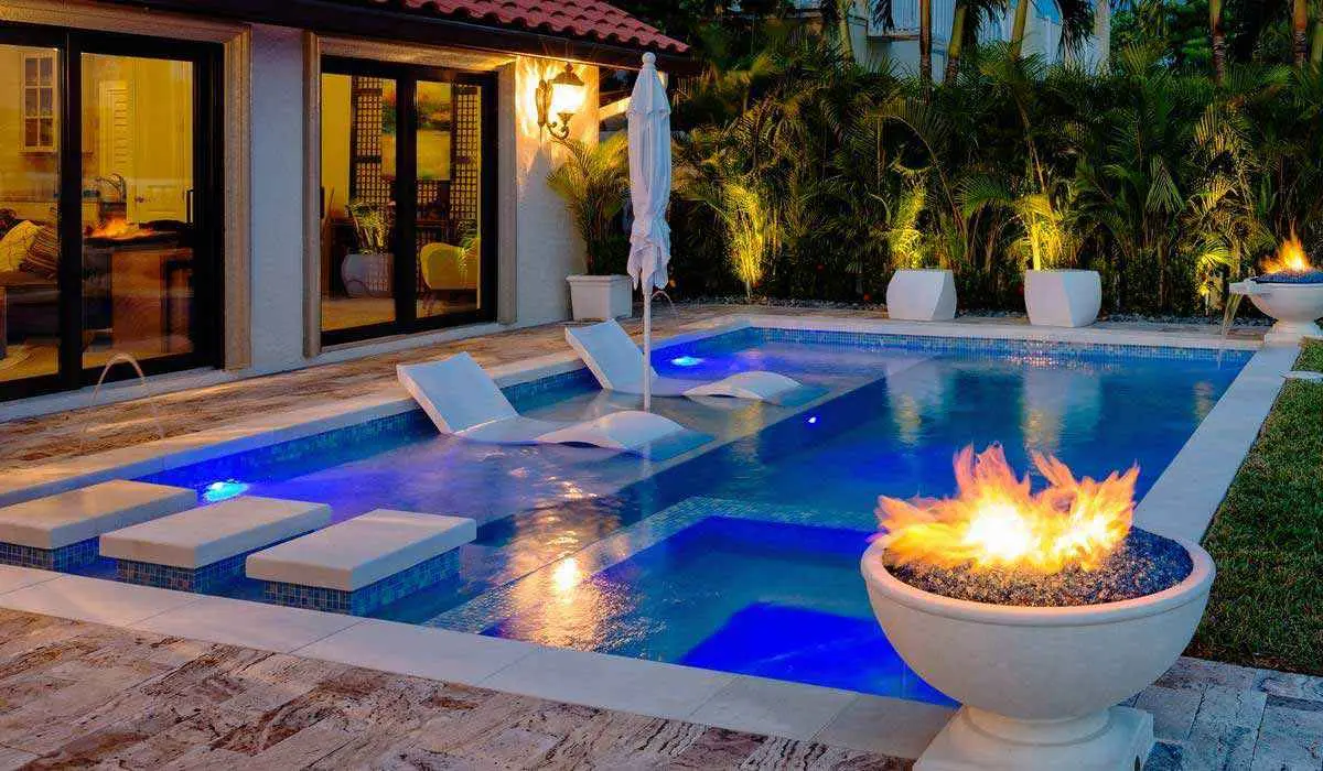 Illuminated resort-style pool with blue water, lounge chairs, fire pit, and tropical landscaping at dusk - Blue Science Pool Service, Tampa, FL