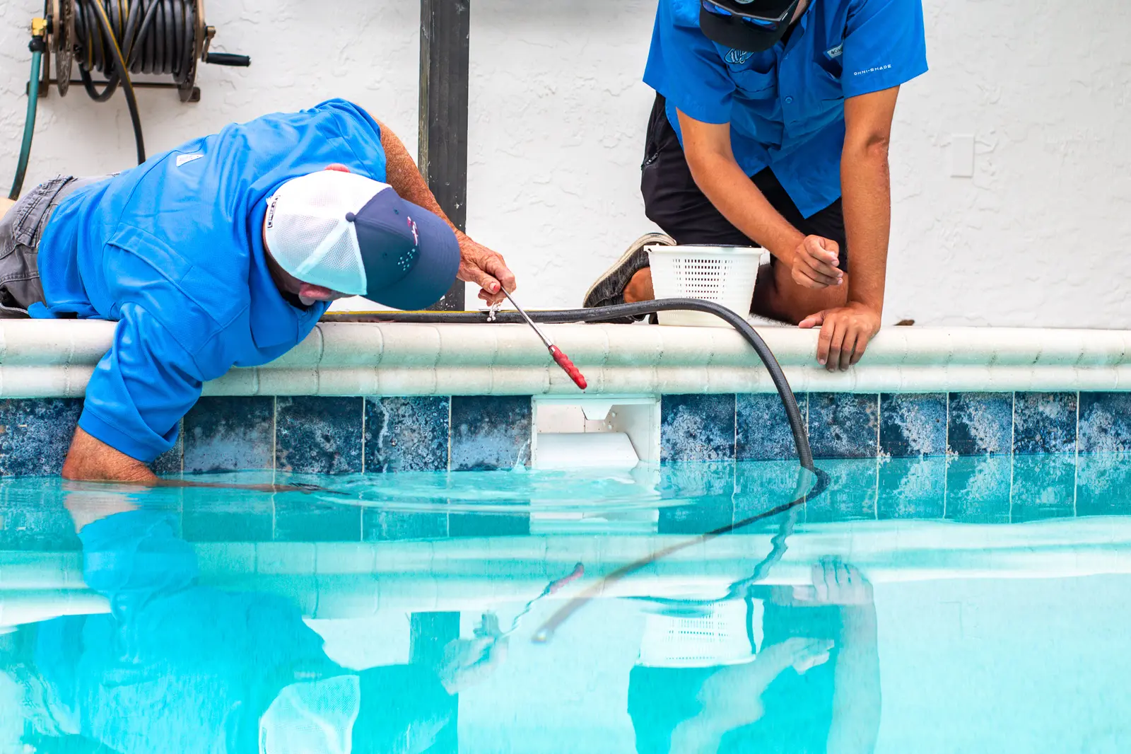 Two technicians in blue uniforms working on pool maintenance with testing equipment - Leak Wizard, Tampa, FL