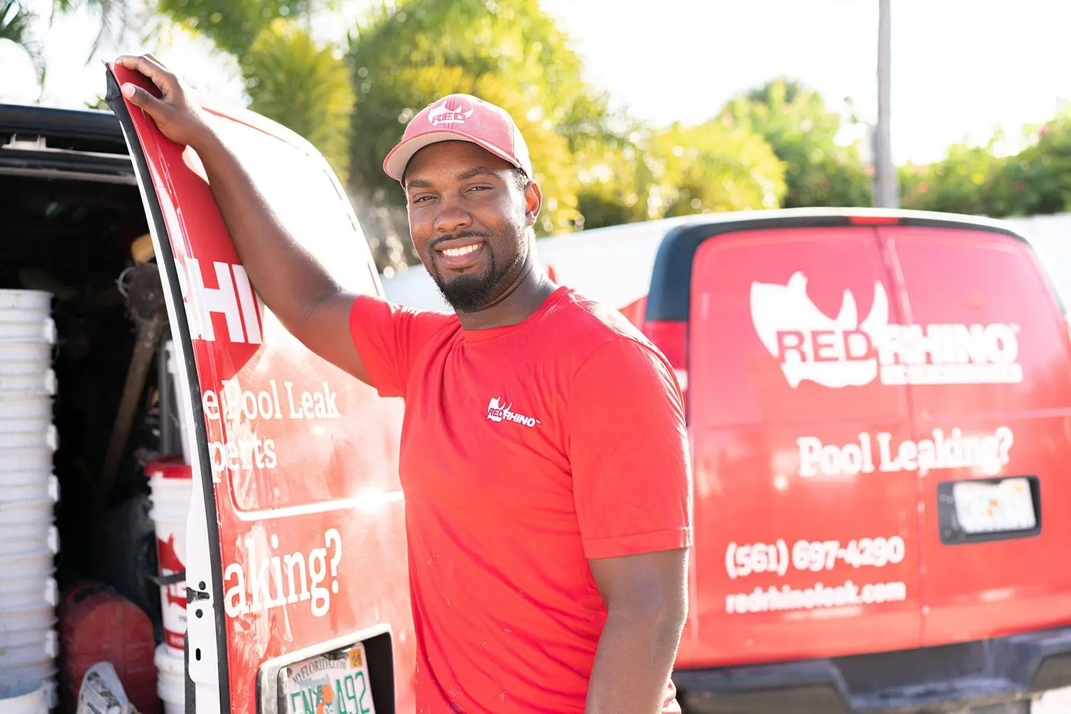 RED RHINO technician in red branded uniform next to red service truck with company logo - RED RHINO, The Pool Leak Experts, Tampa, FL
