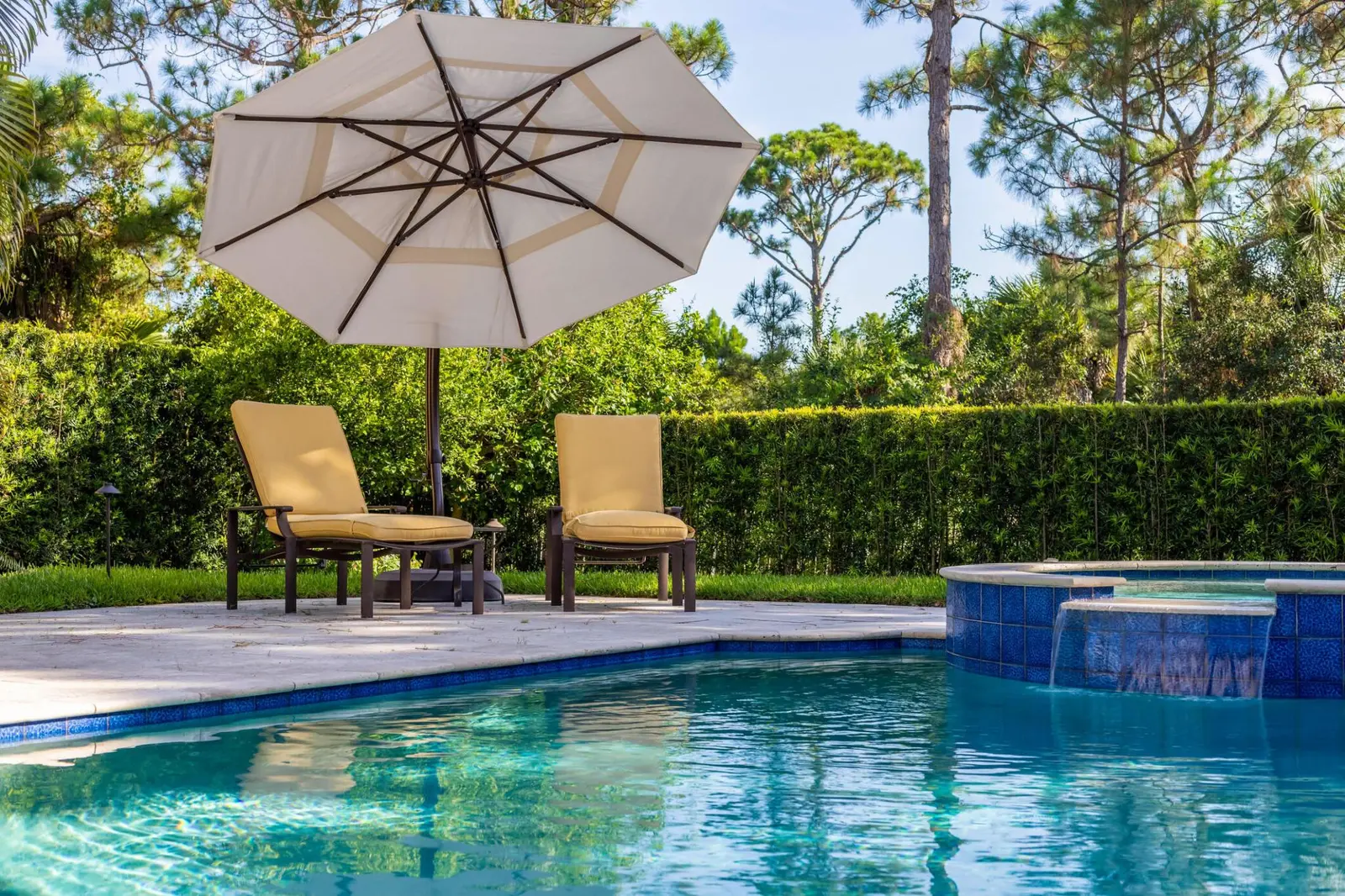 Sparkling clean swimming pool with crystal-clear water, blue tile, and lounge seating under an umbrella - Finn's Pool Services, West Palm Beach, FL