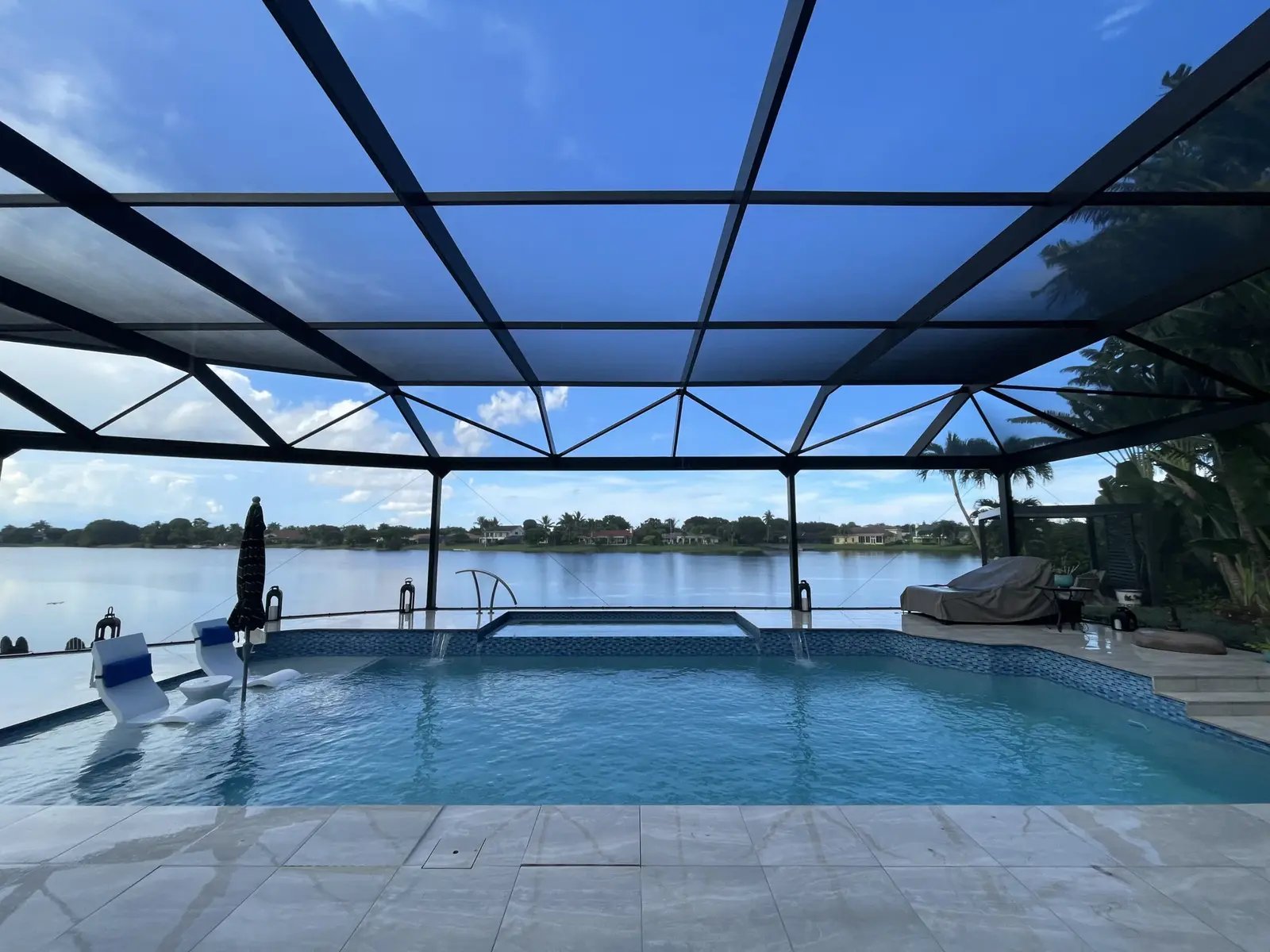 Crystal clear pool with white tile deck under black framed enclosure overlooking waterfront - Finn's Pool Services, West Palm Beach, FL
