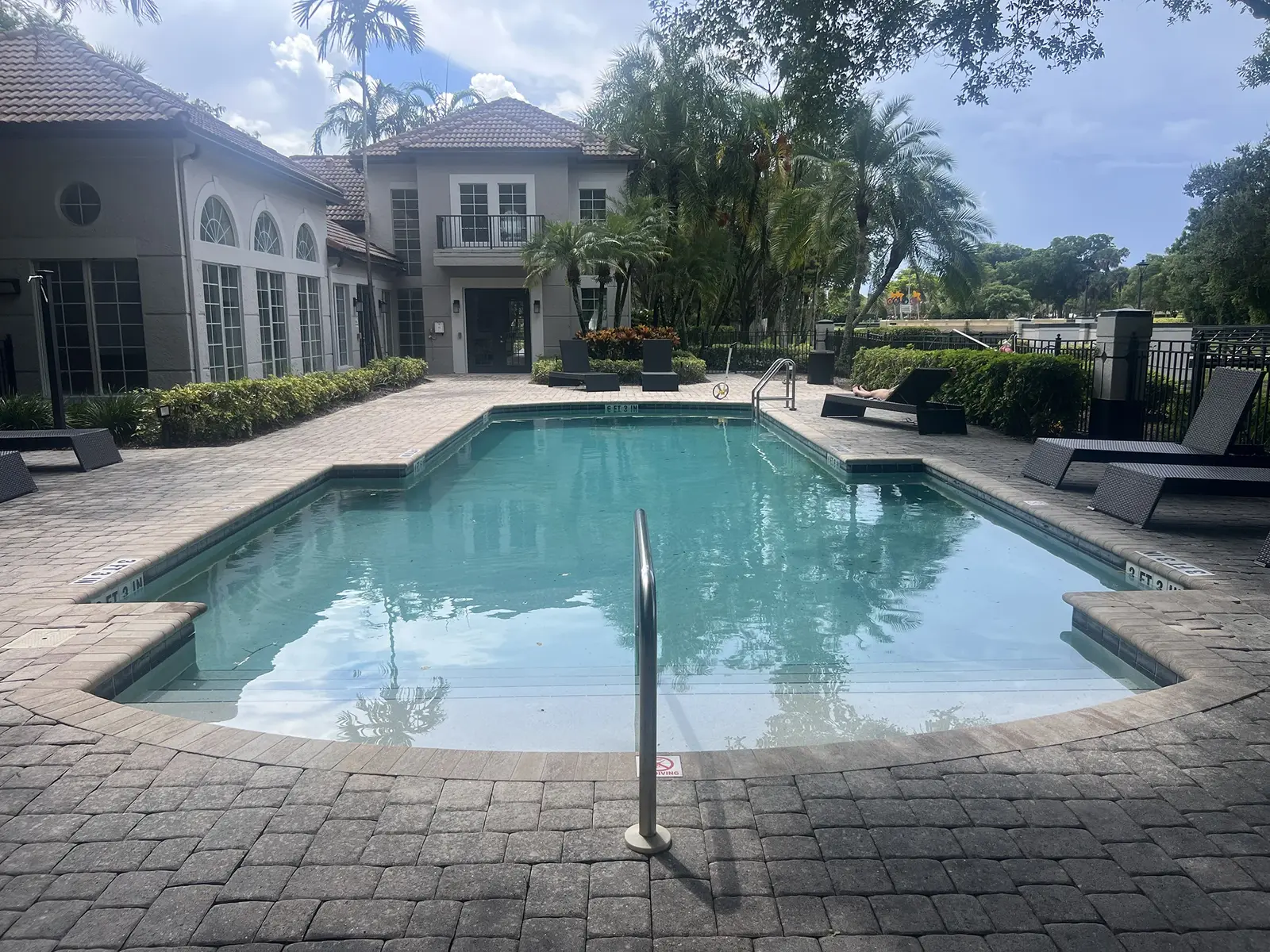 Sparkling turquoise swimming pool with lounge chairs, surrounded by paver deck and luxury home with palm trees - Finn's Pool Services, West Palm Beach, FL