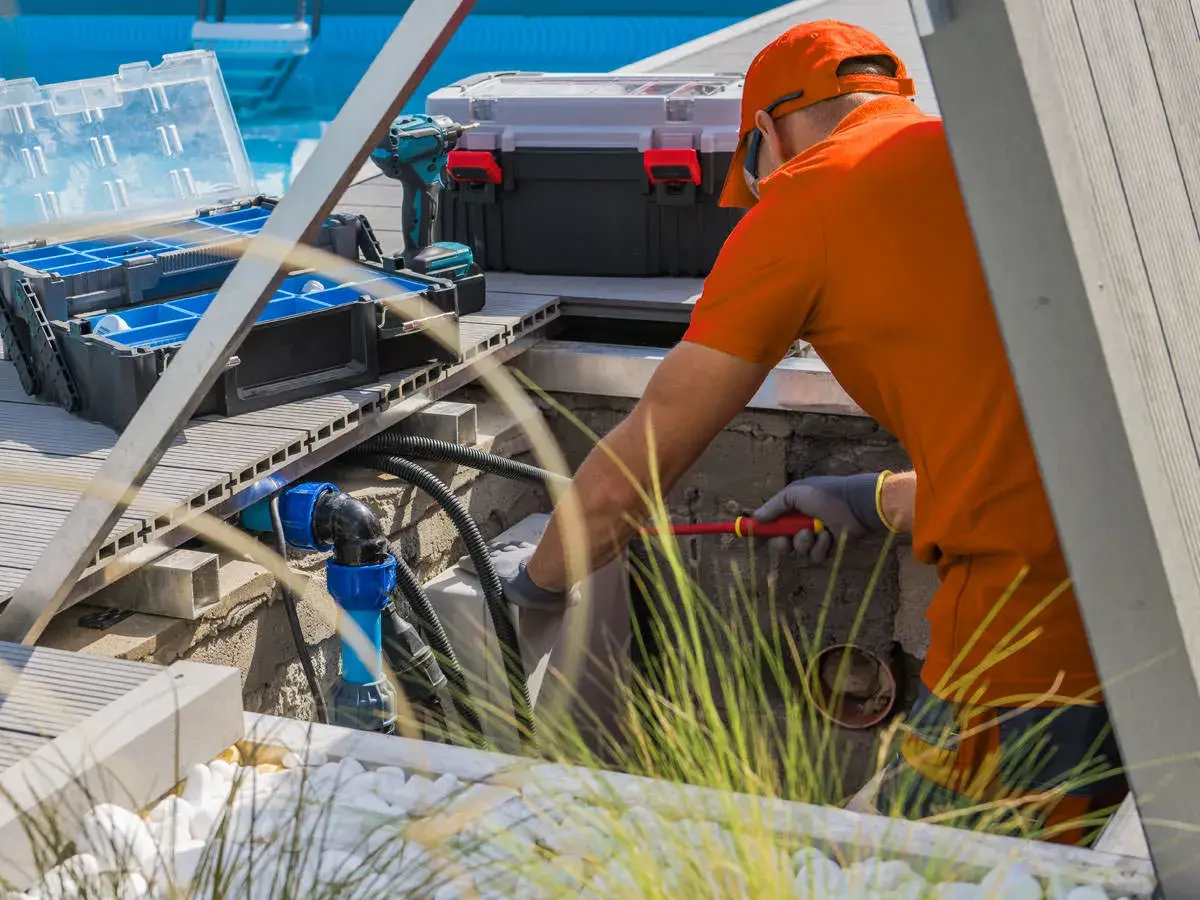 Technician in orange safety gear working on pool equipment and plumbing at poolside - Aaron's Leak Detection, Winter Springs, FL