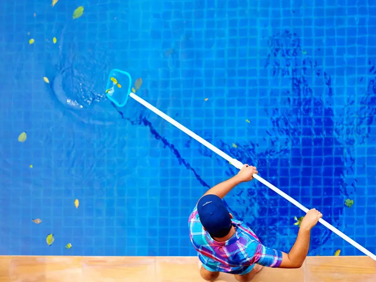 Technician using a net skimmer to clean leaves from a bright blue swimming pool - Aaron's Leak Detection, Winter Springs, FL