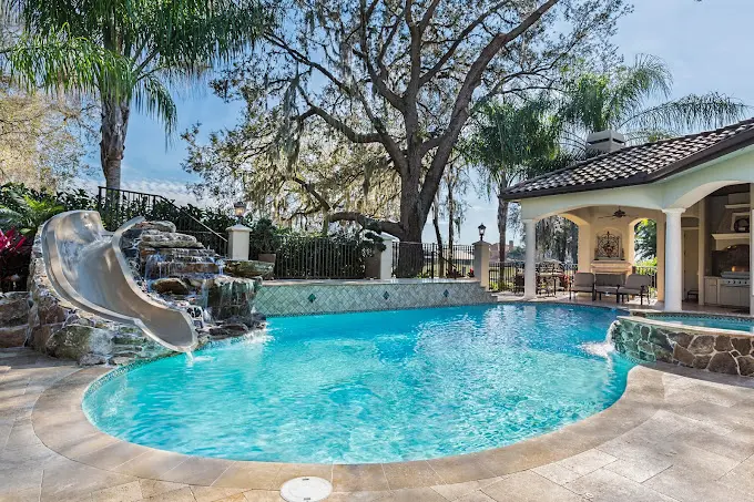 Crystal clear turquoise swimming pool with waterslide, spa, and poolside patio at luxury home - Hill Country Pools, Austin, TX