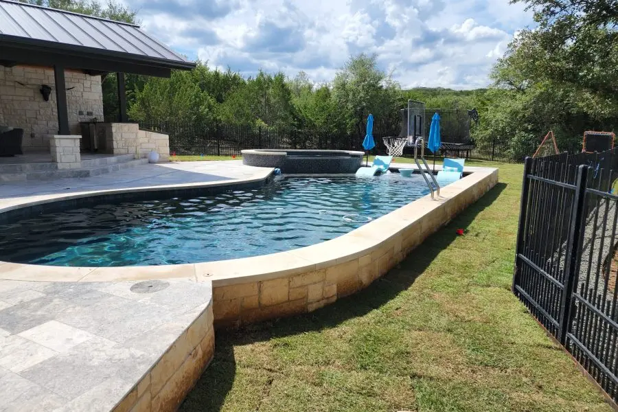 Sparkling blue swimming pool with attached spa surrounded by stone decking and landscaping - Hines Pool & Spa, Austin, TX