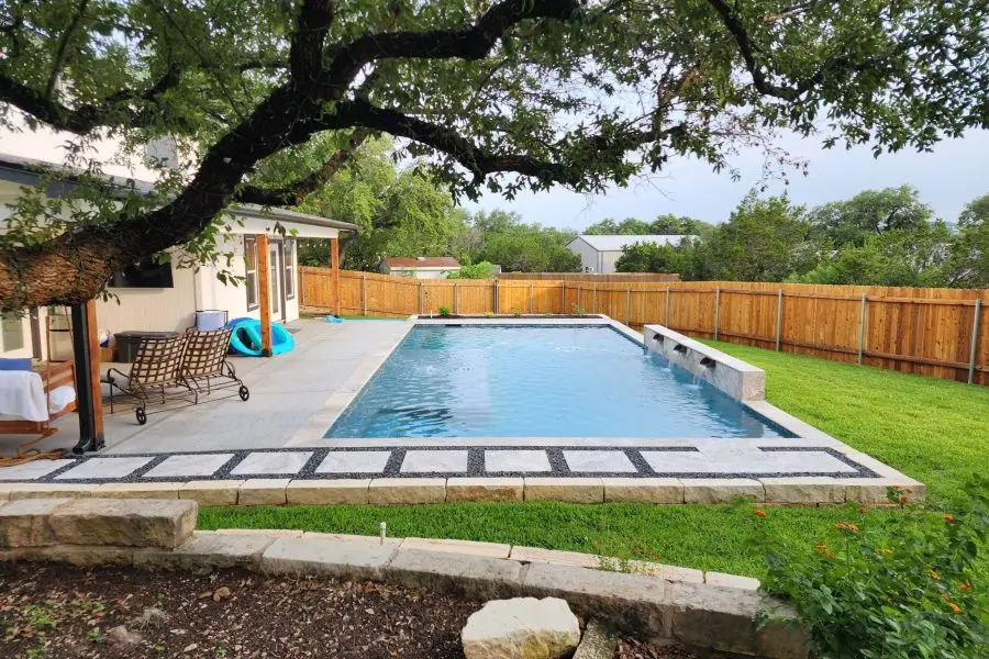 A sparkling blue residential pool with decorative deck paving, surrounded by wooden fence and mature landscaping - Hines Pool & Spa, Austin, TX