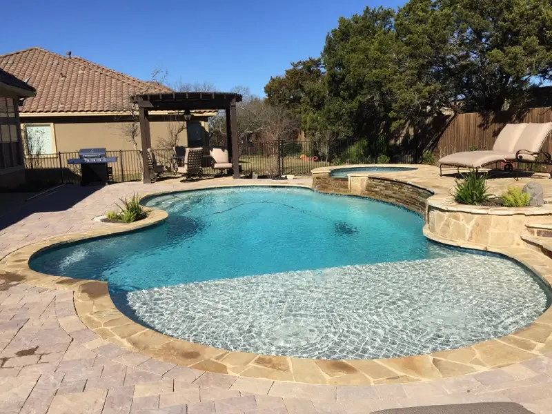 Sparkling clean swimming pool with bright blue water and shallow sun shelf, surrounded by stone deck and lounge chairs - Prime Pool Service, Austin, TX