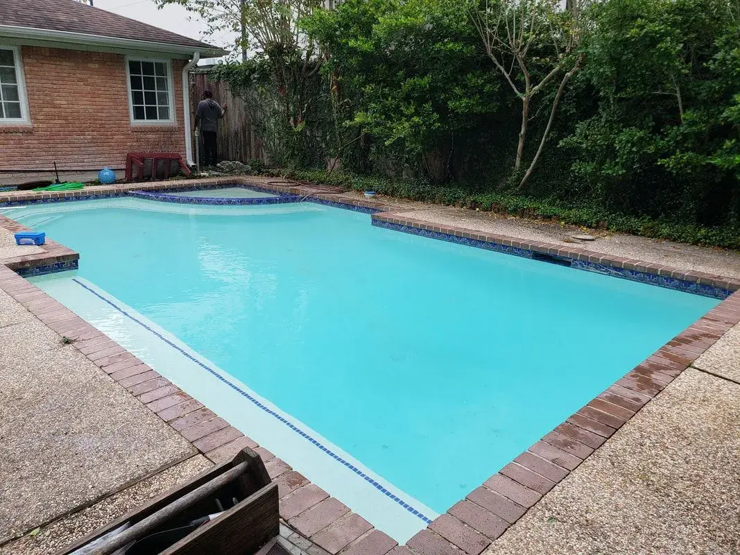 Bright turquoise sparkling clean backyard pool with brick patio and blue tile border - Sweetwater Pool & Patio, Bellaire, TX