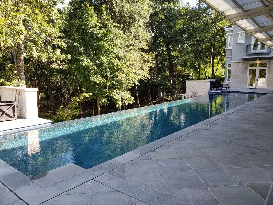 A crystal-clear lap pool with manicured landscaping and stone deck beside a modern house - Sweetwater Pool & Patio, Bellaire, TX