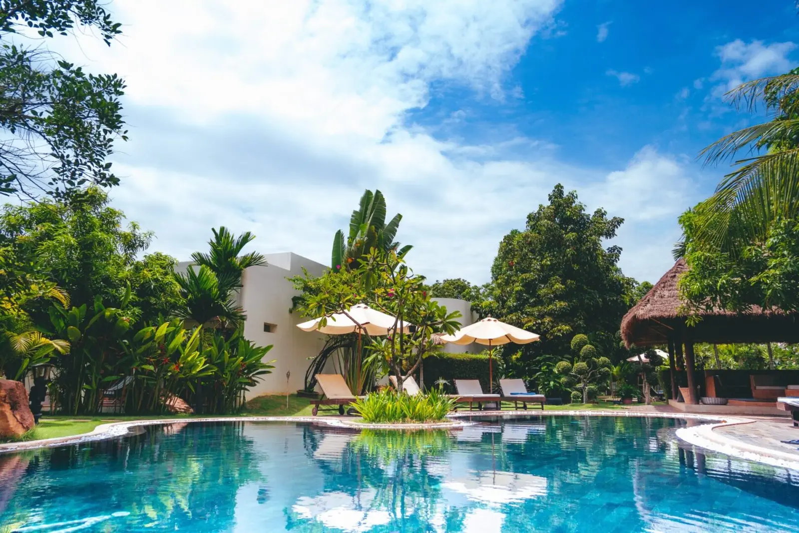 A crystal-clear resort-style swimming pool surrounded by lush tropical landscaping and white umbrellas - Awesome Pool Service, Corpus Christi, TX