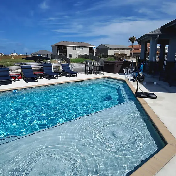 Sparkling blue resort pool with attached spa and lounge seating area on sunny day - Ranch Hand Pool Services, Corpus Christi, TX