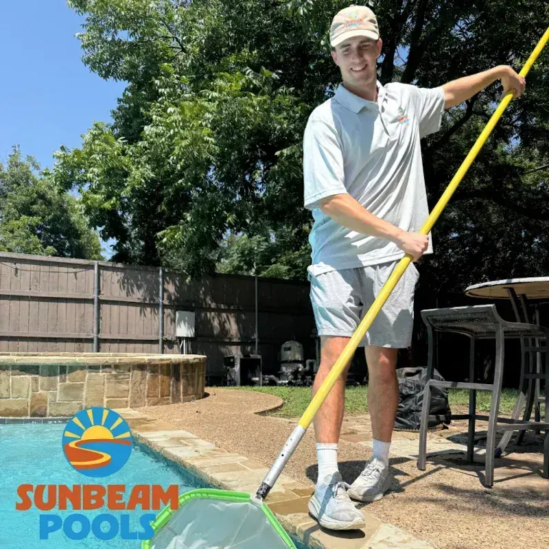 Technician in branded uniform holding pool cleaning equipment by a residential pool - Sunbeam Pools, Dallas, TX