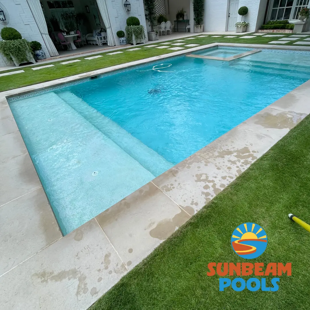 Crystal clear swimming pool with blue tile and white deck, manicured lawn and modern house in background - Sunbeam Pools, Dallas, TX