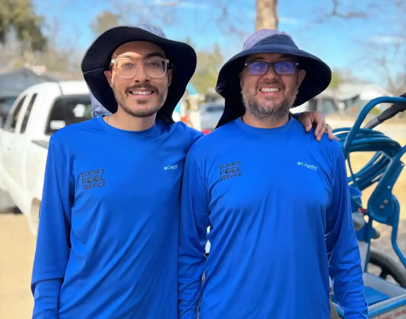 Two smiling Elkin's Pool Service employees in blue branded shirts standing together outdoors - Elkin's Pool Service, Fort Worth, TX