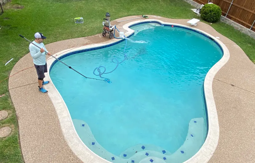 Technician with pool cleaning equipment standing poolside of a bright turquoise residential swimming pool - Elkin's Pool Service, Fort Worth, TX