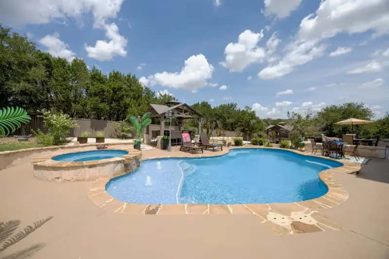 Sparkling blue resort-style pool with spa, stone patio, and landscaped backyard under clear sky - Gary Pools, San Antonio, TX