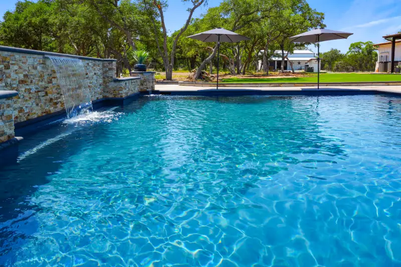 Crystal clear blue swimming pool with stone waterfall feature and manicured grounds - Gary Pools, San Antonio, TX