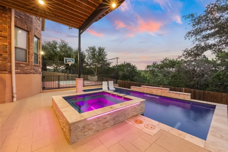 Illuminated custom pool and spa on residential patio at dusk with evening sky - Gary Pools, San Antonio, TX