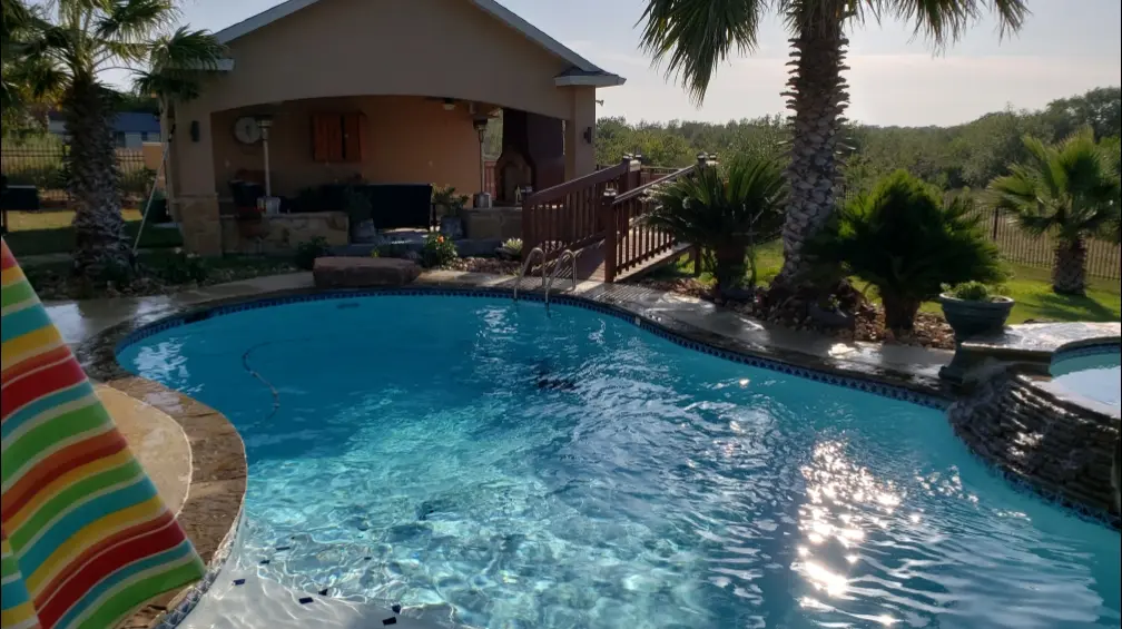 A sparkling clean backyard pool with bright blue water surrounded by palm trees and a poolside patio - Pro-Tech Pool Services, San Antonio, TX